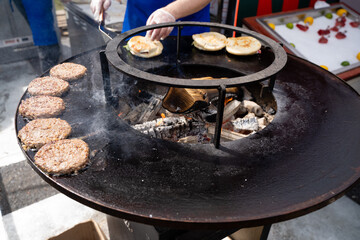 A person is skillfully cooking delicious hamburgers on a grill that is situated over an open fire,...