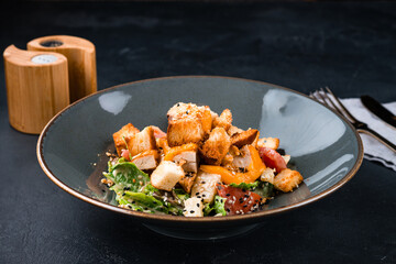 Italian dish Caesar salad with chicken, parmesan cheese, lettuce, tomatoes, croutons on a dark table.