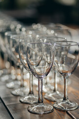 A close-up view of multiple empty wine glasses arranged in rows on a wooden table.