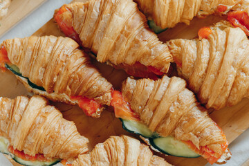 Croissants with cheese cream, red fish and cucumber on wooden board, picnic or outdoors catering