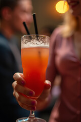 Glass of fresh orange juice with ice cubes and straws, being held in hand, perfect for summer refreshment and healthy lifestyle imagery.