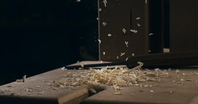 Super slow motion close up of wood chipping shaving pieces with sawdust are falling on workbench after working wood surface with carving tool in artisan carpenter workshop at 1000 fps.