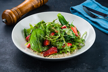 Fresh green salad with strawberries, spinach, arugula, spices, sauce and sesame seeds.