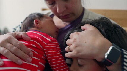 Mother concerned for her older son who appears sick with fever, while cradling a newborn on a couch, showcasing a tender moment of maternal love and care for her children