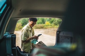 mature japanese woman use mobile phone and sit on the back of her car