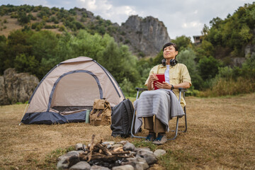Fototapeta premium Mature japanese woman read a book in front of tent on a camping trip