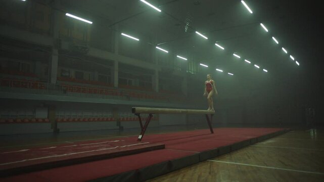 Side view of a Gymnast in red practicing on balance beam