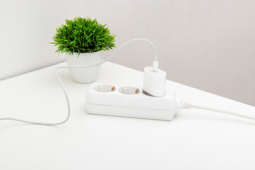 Charging cable in extension cord on white table. Smartphone charging wire