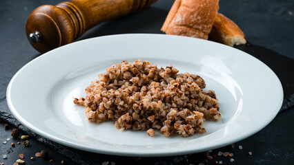 Garnish boiled buckwheat porridge with salt and pepper on a dark background.