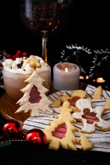 Festive Christmas cookies with icing on a wooden plate, hot cocoa with marshmallows, candle, and holiday decorations in cozy ambiance.