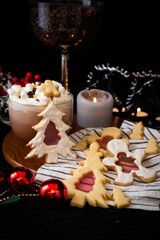 Cozy Christmas arrangement with festive cookies, hot cocoa topped with marshmallows, red ornaments, and candle on a dark background.