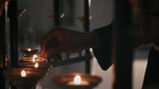 Close up shot of hand of unrecognizable nun lighting up candle with natch in Catholic church