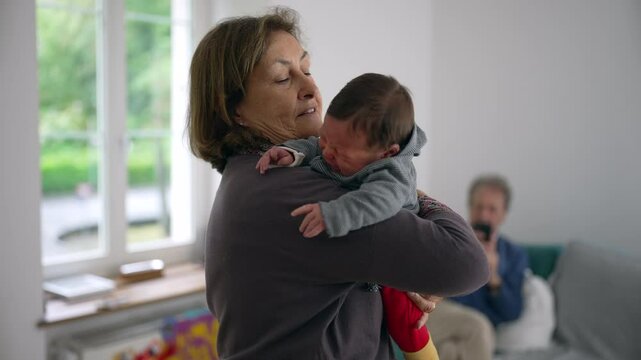Grandmother comforting crying newborn in living room, offering warmth and care, showcasing intergenerational bonding and the nurturing response to a baby&rsquo;s needs in a home setting