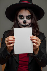 A woman in a Day of the Dead costume with skull makeup and a wide-brimmed black hat holds a blank white sign, perfect for custom Halloween messages or themed promotions.
