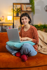 Young Caucasian girl student sitting on sofa finishing laptop work study education at home room. Smiling happy woman freelancer working online, remote job sitting on sofa looking at camera. Vertical