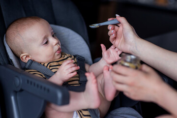 Mother feeding her son in a high chair. Baby's first complementary food