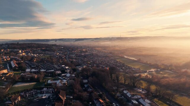 Misty, urban January winters sunset with sun-rays breaking through the mist. Yorkshire aerial scene with red brick houses, industrial buildings, Soft distant mist covering rolling hills and dales.
