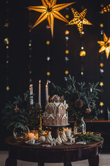 Christmas and New Year beautiful elegant family dinner table setting decorated with candles, fir tree branches, handmade craft toys. Gorgeous big homemade cake with gingerbread houses as centrepiece.