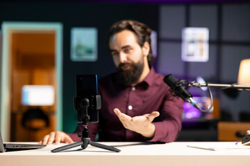 Close up shot of cellphone assessed by tech expert in studio talking about parts used inside. Focus on phone reviewed by entertainer in blurry background for technology internet channel