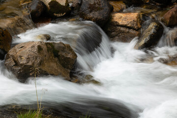 Rushing mountain stream flowing over rocks, creating soft whitewater cascades and splashes