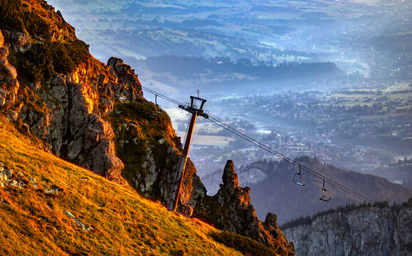 Mountain landscape at sunrise with a cable car system on a rocky slope and a misty valley in the background