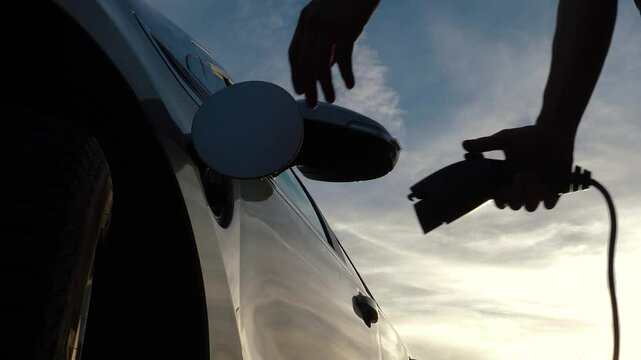 Male hand disconnects charging cable from electric vehicle and finishes charge batteries, clouds in background. Energy electric vehicle. Unrecognizable man unplugs power connector type 1 from EV car