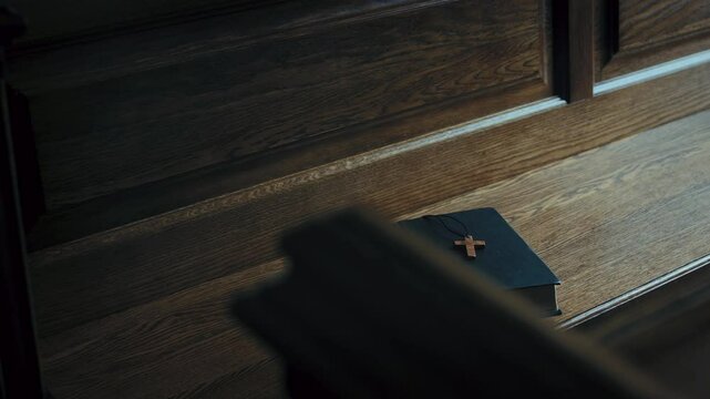 Small Christian cross on rope on holy bible left on wooden bench inside church