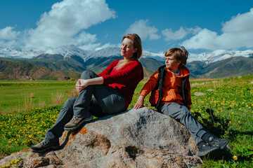 Naklejka premium Mother and son hikers sitting on rock in the mountains on summer day