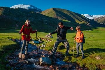 Parents hiking with their son across mountains stream on summer day