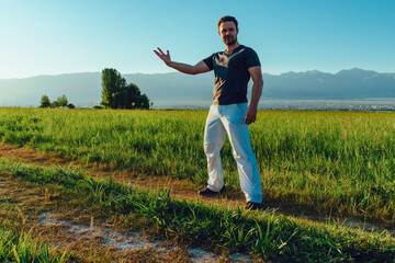 Young strong successful man posing in summer field on mountains background