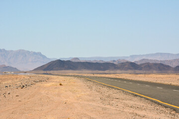 A flat road in the desert in perspective leading to the mountains under the blue sky