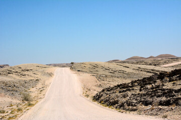 A dirt road in the desert in perspective leading to the hills under a clear blue sky