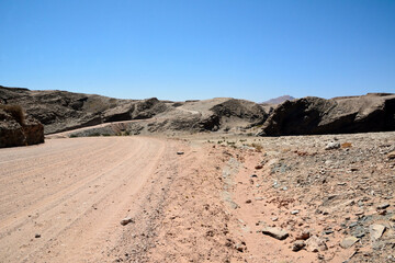 A dirt road in the desert in perspective leading to the hills under a clear blue sky