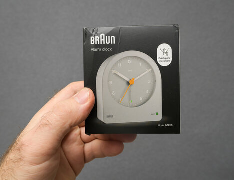 Paris, France - Dec 24, 2024: A male hand holds the gray Braun BC22G alarm clock, designed by German designer Dieter Rams, featuring a quiet quartz movement against a gray background
