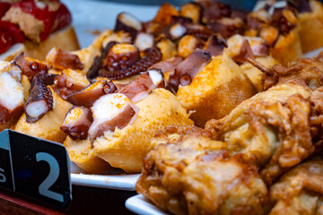 Typical snacks of Basque Country, variety of pinchos or pinxtos oven baked sea food, bread, skewers with jamon, goat cheese served in bar in San-Sebastian or Bilbao, Spain, close up