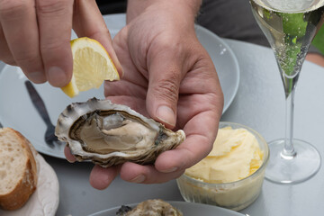 Hand with fresh live oyster, with citron, bread, butter and white wine served at restaurant in oyster-farming village, Arcachon bay, Gujan-Mestras port, France