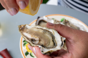 Hand with fresh live oyster, with citron, bread, butter and white wine served at restaurant in...