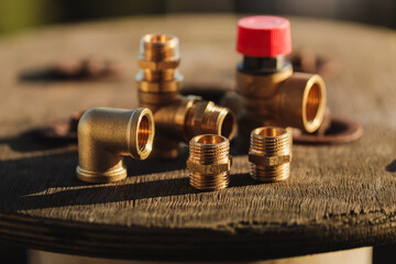 Brass plumbing fittings lying on a rustic wooden table on a sunny day (selective focus)