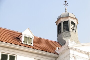 The historic rooftop and tower of Fatahillah Museum in Jakarta, showcasing Dutch colonial architecture with its red-tiled roof and iconic bell tower under a clear blue sky