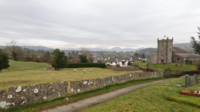 St Michael & All Angels Church in Hawkshead, showing fields and grazing sheep Cumbria,