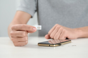 Man with SIM card near smartphone at white table indoors, closeup