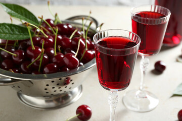 Delicious cherry liqueur in glasses and fresh berries on light grey table
