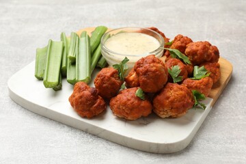 Baked cauliflower buffalo wings with celery and sauce on grey textured table, closeup