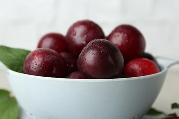 Ripe plums in colander on table, closeup