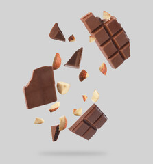 Pieces of tasty chocolate and hazelnuts in air on light grey background
