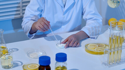 Fototapeta premium A researcher is stirring cream in a petri dish, surrounded by a dish of cream and lemon ingredients in glassware on a table. Laboratory background with blue light