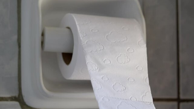 Close up of a hand unrolling and pulling a roll of toilet paper in a white-tiled bathroom, slow motion