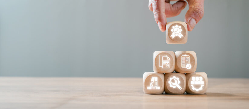 Wooden blocks with icons symbolizing ISO 9001 certification, quality management, standards, and continuous improvement in a business context.