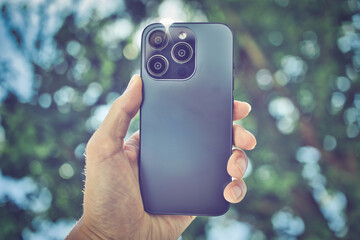 スマホを持つ人の手と木の緑ぼかし