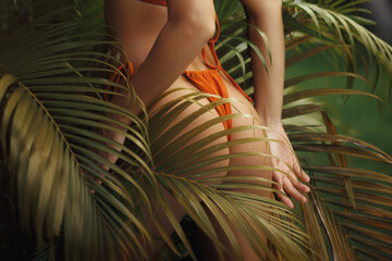 Close-Up of Woman's Curves in Orange Bikini Among Tropical Palm Leaves